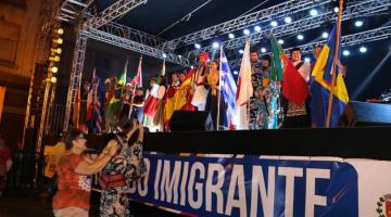 Pessoas com bandeiras de diversos países em cima de palco #paratodosverem