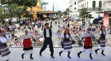 Dançarinos típicos se apresentam de costas para o público com Museu Pelé e Estação do Valongo ao fundo. #pracegover