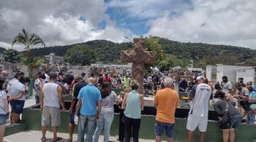 Pessoas rezando na frente de uma cruz no cemitério #paratodosverem