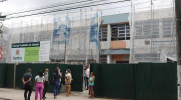 visitantes estão parados em porta de escola coberta por manta de proteção porque a fachada está em obras. #paratodosverem