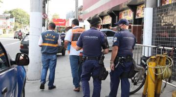 Guardas municipais e fiscais de finanças andam em calçada ao lado de estabelecimento comercial #Paratodosverem