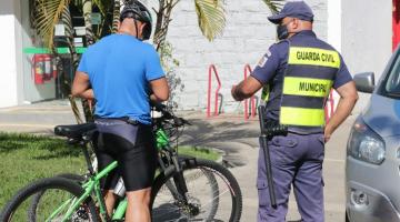 Guarda municipal está ao lado de ciclista. Ambos estão de costas. #Paratodosverem