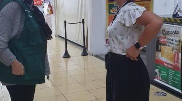 Fiscal conversa com mulher em área de alimentação de shopping