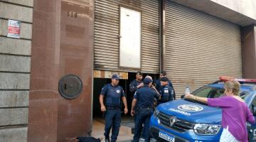 viatura da guarda está parada na porta de estabelecimento com porta semi-cerrada. Guardas estão na frente. #paratodosverem