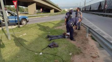 Viatura da guarda municipal parada à esquerda. Guarda e policiais estão em pé ao lado de homem deitado que está dominado. #paratodosverem