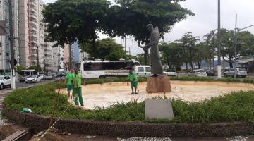 três operários uniformizados estão dentro de área da fonte, sem água. A estátua de santo antônio está ao centro. A área da fonte é rodeada por vegetação. #paratodosverem