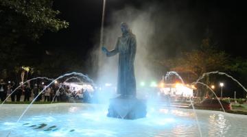 Fonte iluminada com a estátua de Santo Antônio ao centro. #pratodosverem