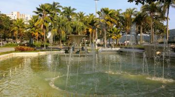 Vista geral de praça com chafariz e palmeiras ao fundo. #paratodosverem 