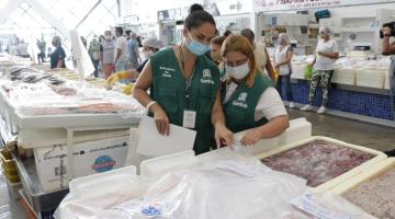 Duas fiscais observam caixas de isopor com pescados. #Paratodosverem