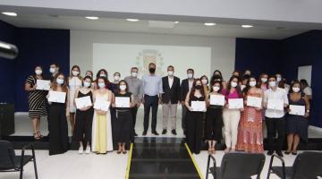 grupo de formandos posa para foto reunido em auditório. Ao fundo, o brasão de Santos está projetado num telão. #paratodosverem