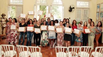 Formandas estão em pé, todas juntas, exibindo seus certificados de curso. #Pracegover