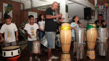 Jovens e um adulto fazem apresentação de percussão. #Pracegover