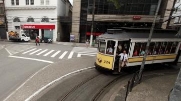 Faixas de segurança para pedestres ao fundo. Bonde turístico está passando ao lado direito da imagem. #Pracegover