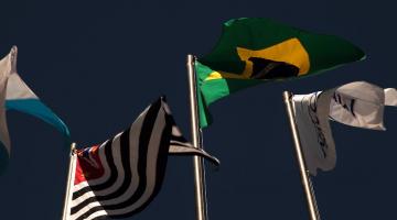 da esquerda para a direita, as bandeiras de São Paulo, Brasil e Mercosul tremulando sob o céu azul. #paratodosverem