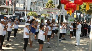 pessoas praticam tai chi chuan em praça. ambiente está decorada com luminárias orientais. #paratodosverem 