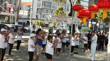 Praticantes fazem tai chi chuan em área ao ar livre. #Pracegover