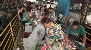 Linha de reciclagem com catadores fazendo a separação #pracegover. 