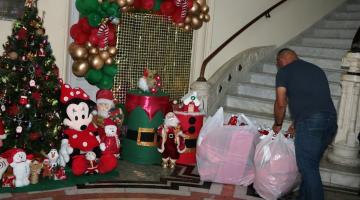 salão com decoração de natal e um homem de costas para a foto acomodando dois grande sacos com presentes. #paratodosverem 