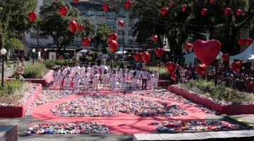 milhares de corações de tecido dispostos no chão da praça mauá, com pessoas vestidas de branco e de mãos dadas ao fundo. Em primeiro plano, decoração de corações pendurados em fios. #paratodosverem 