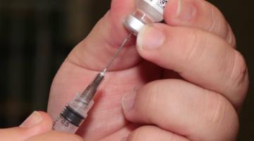 #pracegover enfermeiro insere agulha de seringa em frasco de vacina