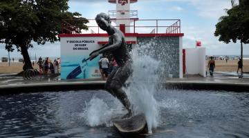 a fachada da escola de surfe com a estátua de surfista na água em primeiro plano. #paratodosverem 