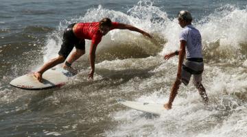 dois jovens estão surfando onda frente a frente. #paratodosverem 