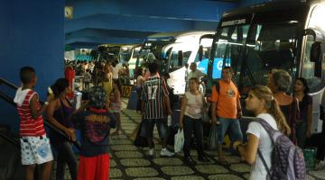 Pessoas transitando perto dos ônibus parados na rodoviária #pracegover 