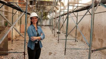 viviane está em pé, de braços cruzados, em ambiente de obra, com andaimes dos dois lados. #paratodosverem