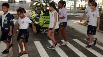 crianças atravessam a rua da minicidade de frente pra bugue que aguarda #paratodosverem