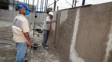 dois homens realizam trabalho em muro de escola #paratodosverem