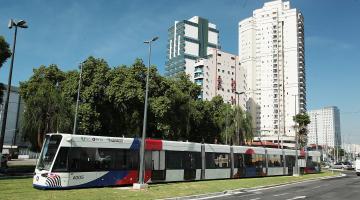 Vista geral do VLT sobre trilho em avenida. #Paratodosverem