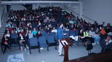 público está sentado em um auditório assistindo palestra de um homem que fala ao microfone à frente de todos. #paratodosverem 