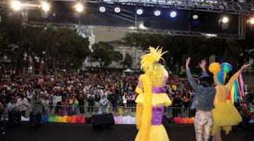 pessoas na praça acompanhando show com pessoas fantasiadas no palco #paratodosverem