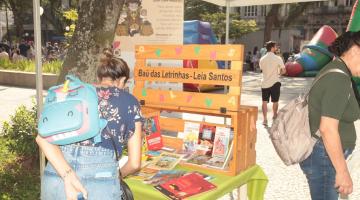 mulher de costas para foto mexe em livros dispostos sobre um estande. #paratodosverem 