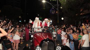 papai e mamãe noel está dentro de calhambeque. Grande público está em torno acenando. #paratodosverem