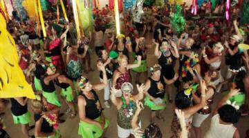 salão decorado com motivos de carnaval e pessoas dançando. #paratodosverem 