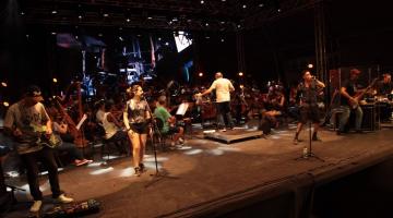 sinfônica está tocando em palco com músicos cantando à frente. #paratodosverem