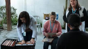 agentes de saúde atendem pessoas em salão. #paratodosverem