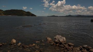 vista do mar com pedras em primeiro plano e geobag ao fundo. #paratodosverem 