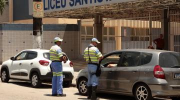 dois agentes de trânsito estão próximo a um carro que está parado na porta de uma escola. #paratodosverem