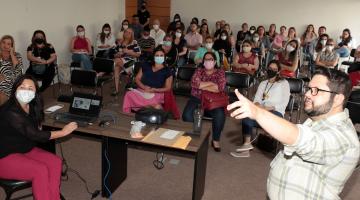 palestrante fala e pessoas sentadas em auditório acompanham #paratodosverem