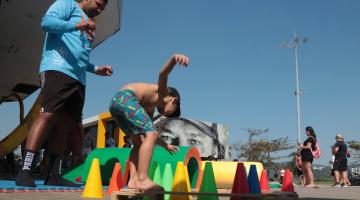 menino brinca de se equilibrar entre cones. O pai observa.#paratodosverem