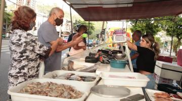 pessoas comprando peixe em barraca localizada em rua #paratodosverem