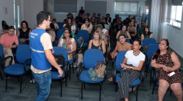 servidores estão sentados em pequeno auditório atentos a um outro servidor que está em pé, de costas para a foto. #paratodosverem