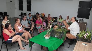 professor fala às alunas com orquideas na mesa #paratodosverem  