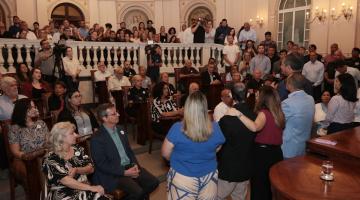 sala lotada com pessoas sentadas e em pé #paratodosverem