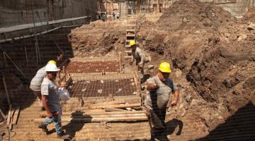 homens estão trabalhando em terreno. eles mexem em estruturas de ferro. #paratodosverem