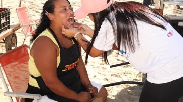 mulher examina boca de outra mulher que está sentada. #paratodosverem