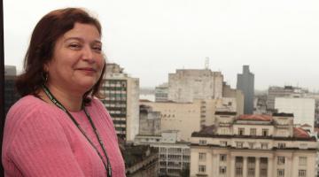 monica posa para foto em uma janela, com o palácio josé bonifácio ao fundo. #paratodosverem