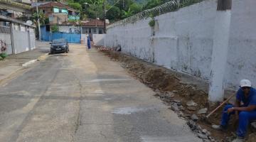 rua com calçadas quebradas à direita. ao fundo, um carro estacionado à esquerda, e um homem caminhando no leito carroçavel. #paratodosverem 